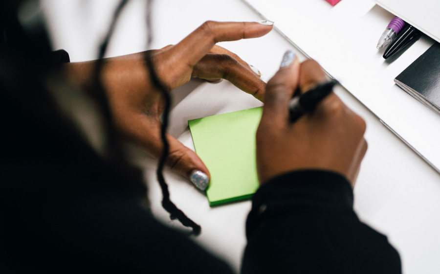 Close up of a black person’s hands writing on a post-it Post it note