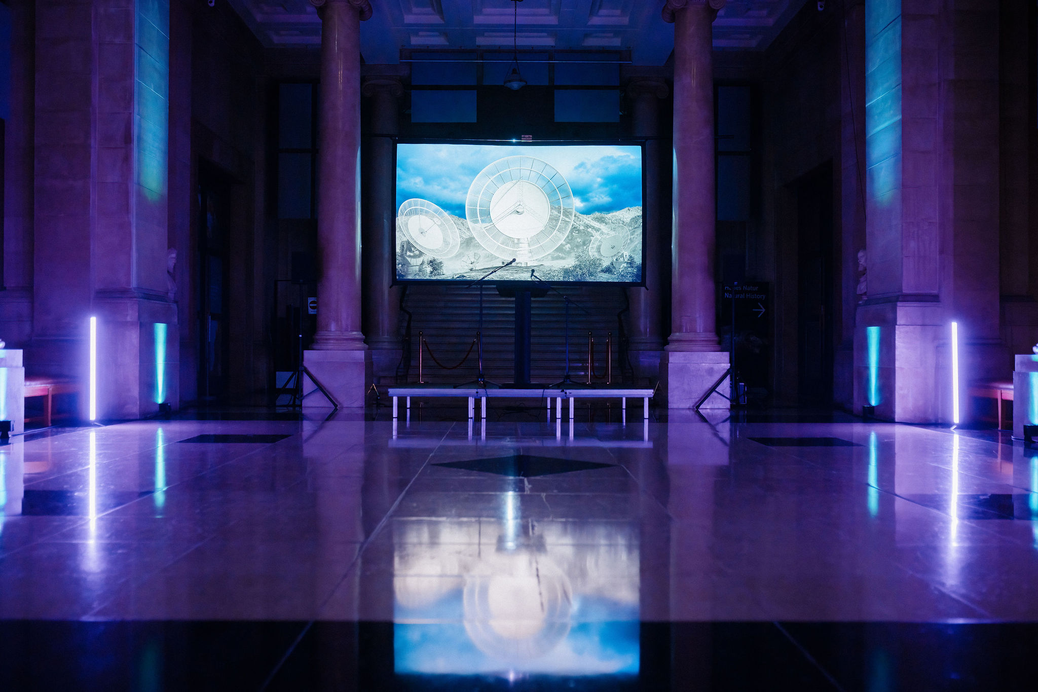A screen displaying an image of a broadcast satelite in a room dimly lit with purple lights