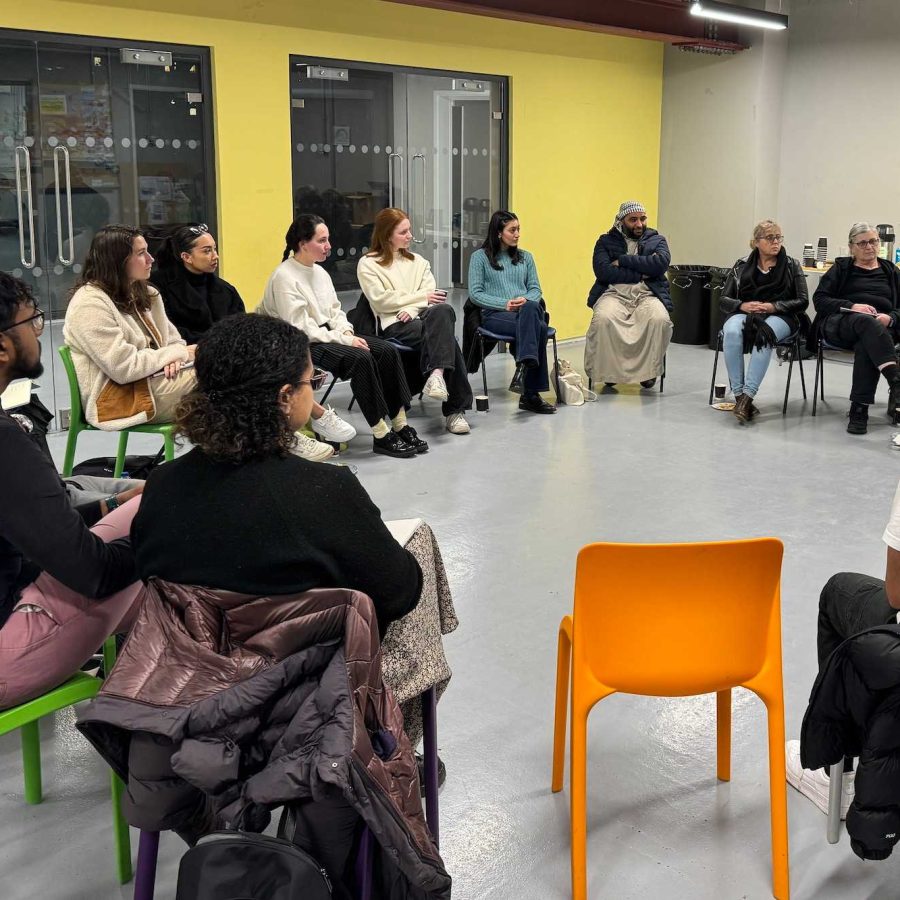 A diverse group of people seated in a circle talk in a hall