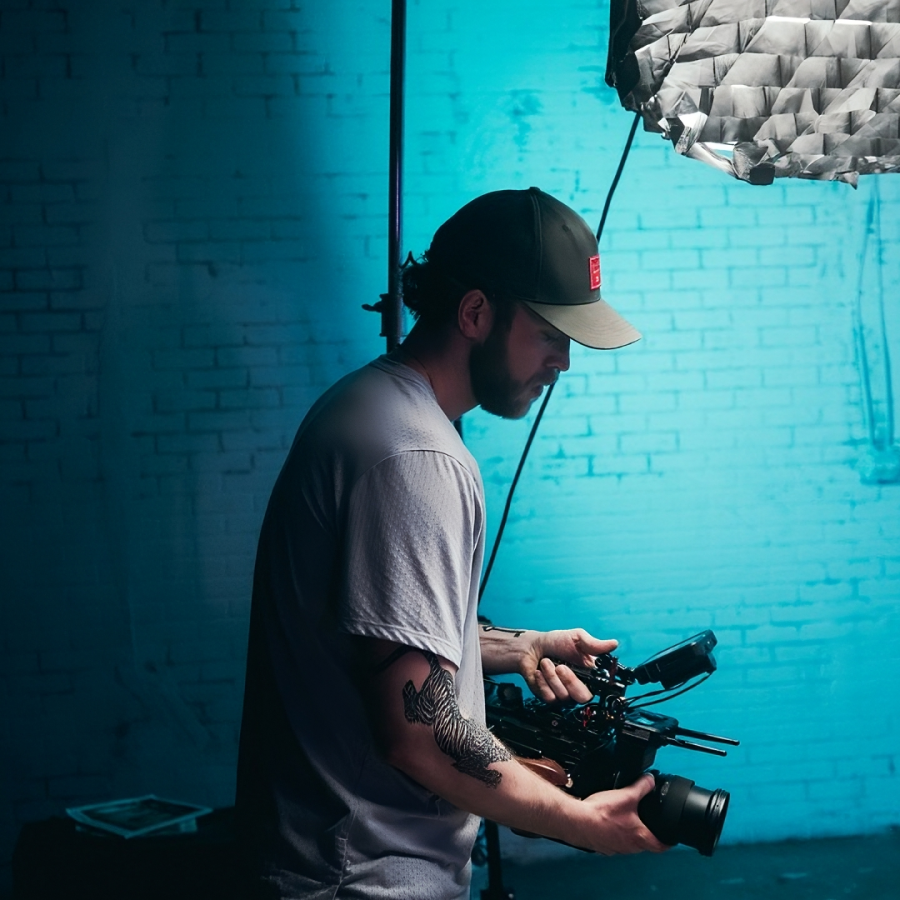 Freelancer holding a video camera against a blue brick background with a lighting rig