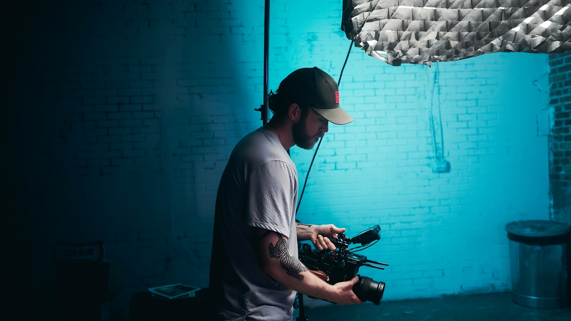 Freelancer holding a video camera against a blue brick background with a lighting rig